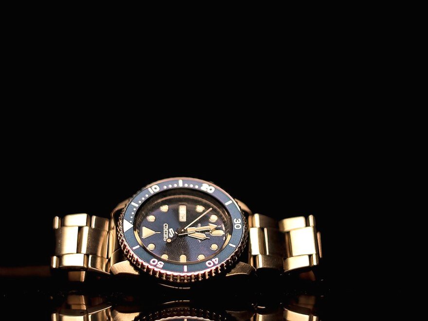 A gold wristwatch with a dark dial on a reflective surface